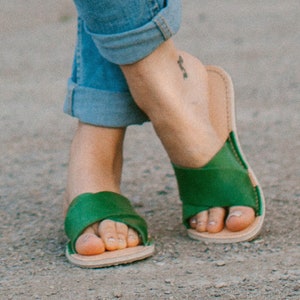 May include: A pair of green leather sandals with a simple design. The sandals have a flat sole and a strap that goes across the top of the foot.