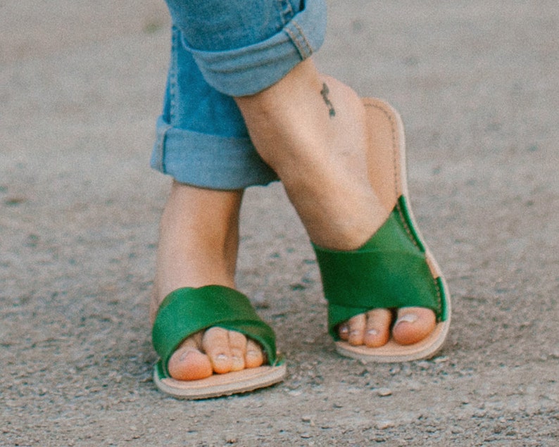 May include: A pair of green leather sandals with a simple design. The sandals have a flat sole and a strap that goes across the top of the foot.