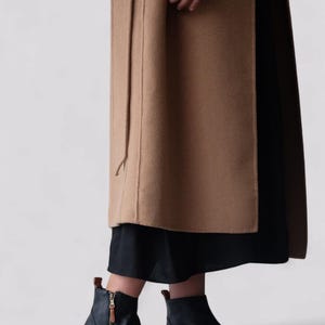 Pu&ograve; includere: Stivali neri in pelle con cerniera laterale e punta arrotondata. Gli stivali sono indossati con un cappotto marrone e una gonna nera.