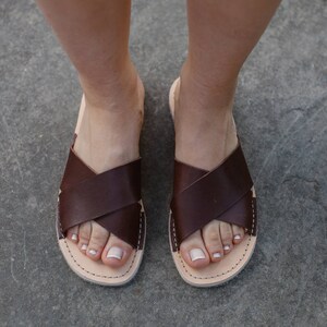 May include: A pair of brown leather sandals with a criss-cross strap design. The sandals have a simple, minimalist style and are perfect for warm weather.