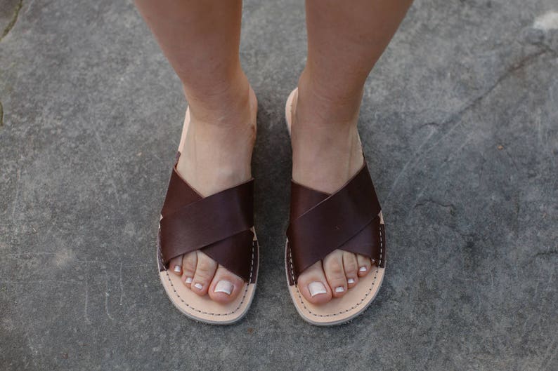 May include: A pair of brown leather sandals with a criss-cross strap design. The sandals have a simple, minimalist style and are perfect for warm weather.