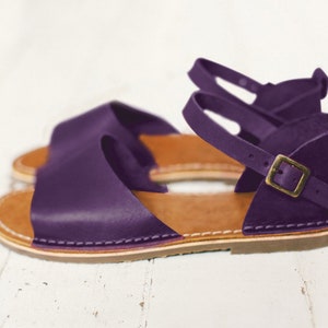 May include: Purple leather sandals with a buckle fastening and a brown sole.