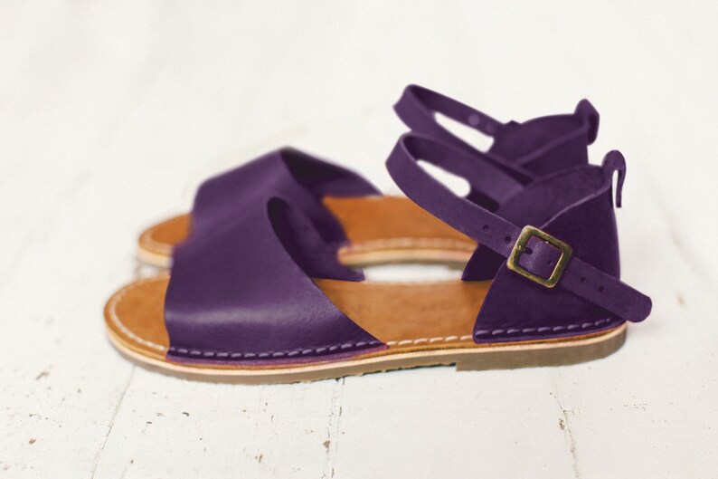 May include: Purple leather sandals with a buckle fastening and a brown sole.