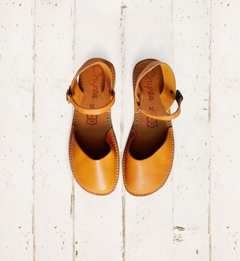 May include: A pair of tan leather sandals with ankle straps. The sandals have the word "Crypon" written on the straps and the size "38" is printed on the inside of each sandal.