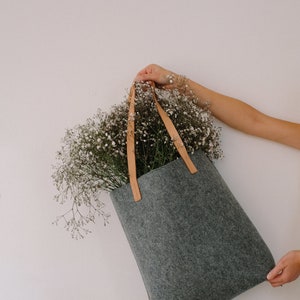 May include: A gray felt tote bag with brown leather straps, filled with a bouquet of white baby's breath flowers.