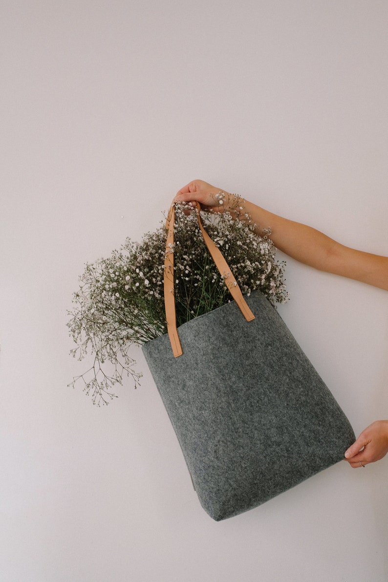May include: A gray felt tote bag with brown leather straps, filled with a bouquet of white baby's breath flowers.
