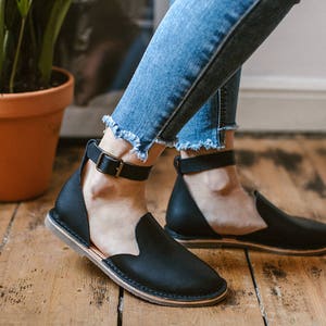 May include: A pair of black leather ankle strap sandals with a low heel. The sandals have a simple design and are made of high-quality leather.