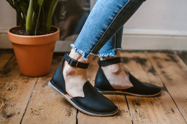May include: A pair of black leather ankle strap sandals with a low heel. The sandals have a simple design and are made of high-quality leather.