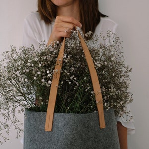 May include: A gray felt tote bag with brown leather straps, filled with a bouquet of white baby's breath flowers.