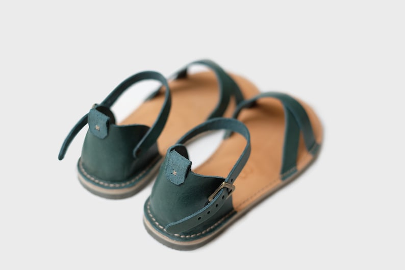 May include: A pair of teal blue leather sandals with adjustable straps and buckles. The sandals have a flat sole and are made of a soft, supple leather.