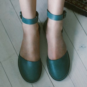 May include: A pair of teal blue leather sandals with ankle straps and a simple design.