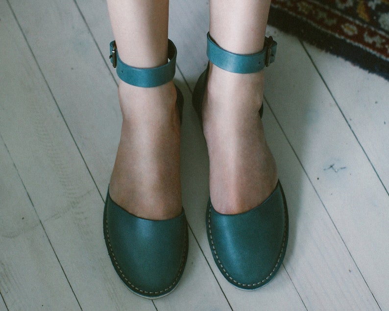 May include: A pair of teal blue leather sandals with ankle straps and a simple design.