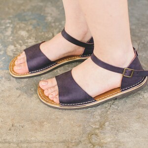 May include: A pair of dark purple leather sandals with a buckle fastening and a brown leather sole.