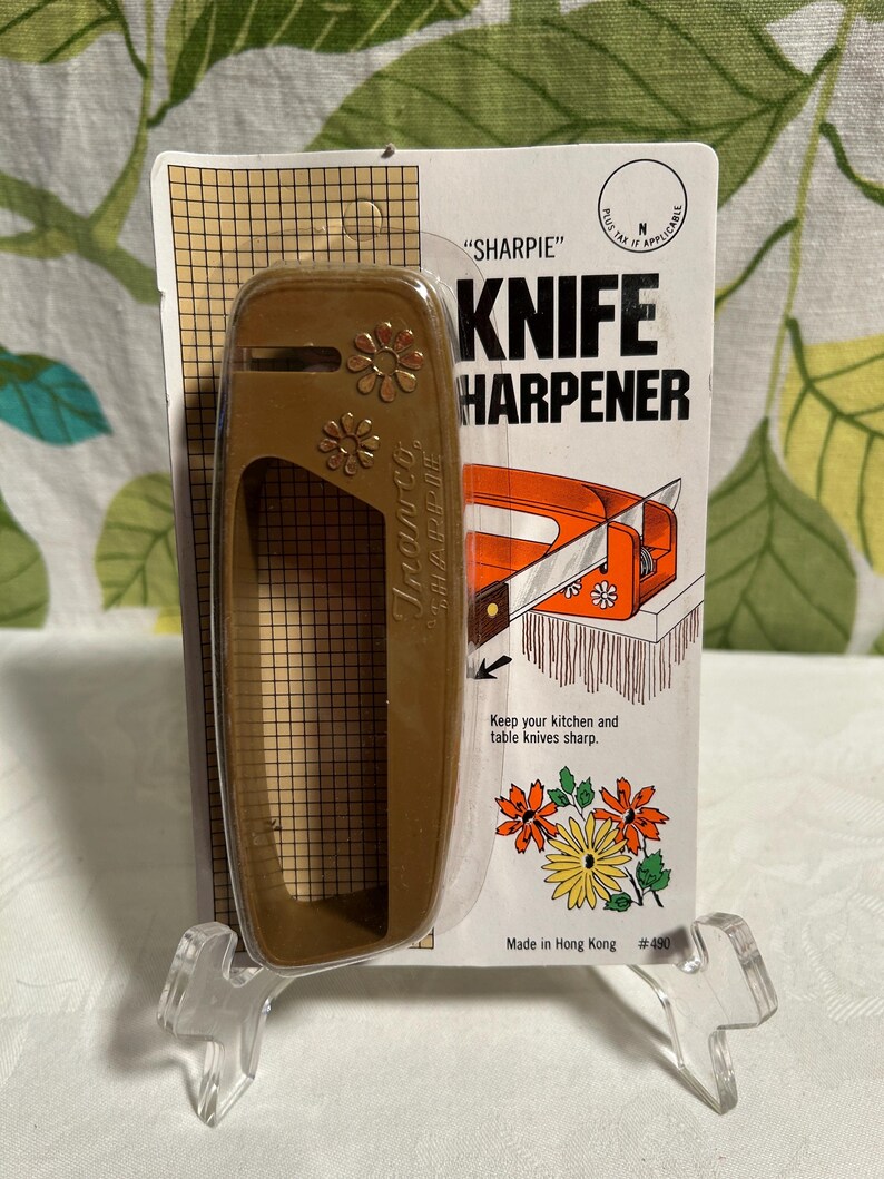 Pode incluir: Um afia-facas de pl&aacute;stico castanho com um design floral. A embalagem diz "SHARPIE" KNIFE HARPENER. Diz "Keep your kitchen and table knives sharp." e "Made in Hong Kong #490".