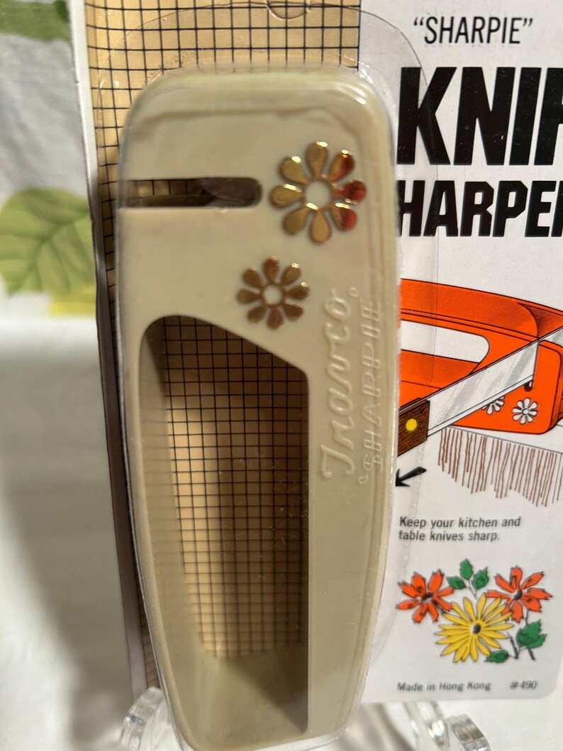 May include: A beige plastic knife sharpener with a gold flower design. The packaging says "SHARPIE" KNIF HARPER and "Keep your kitchen and table knives sharp." It also says "Made in Hong Kong #490".