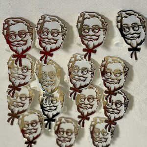 May include: A collection of 13 white plastic figurines of a man with a mustache and glasses. The figurines are all in the same pose, with the man's head tilted slightly to the side. The figurines are all wearing a bow tie and have a gold metallic finish.
