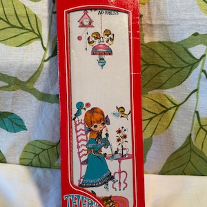 May include: A tall, rectangular red box for a telephone and address book. The front features a white panel with a cartoon illustration of a person writing at a table, birds, a clock, and the text "ADDRESS" and "TELEPHONE AND ADDRESSES".