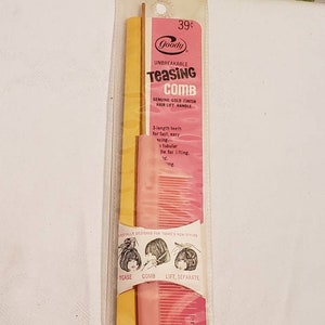 May include: A pink and gold teasing comb with a gold handle and a pink comb with gold teeth. The comb is packaged in a clear plastic wrapper with the brand name "Goody" and the text "Unbreakable Teasing Comb" printed on it. The comb is designed for teasing, combing, lifting, and separating hair. The text "39¢" is printed on the package.
