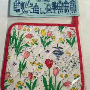 May include: A quilted pot holder with a red border and a white background featuring a tulip and windmill design. The packaging reads "POT HOLDER TOPFLAPPEN" and "HOLLAND". Made of 100% cotton.