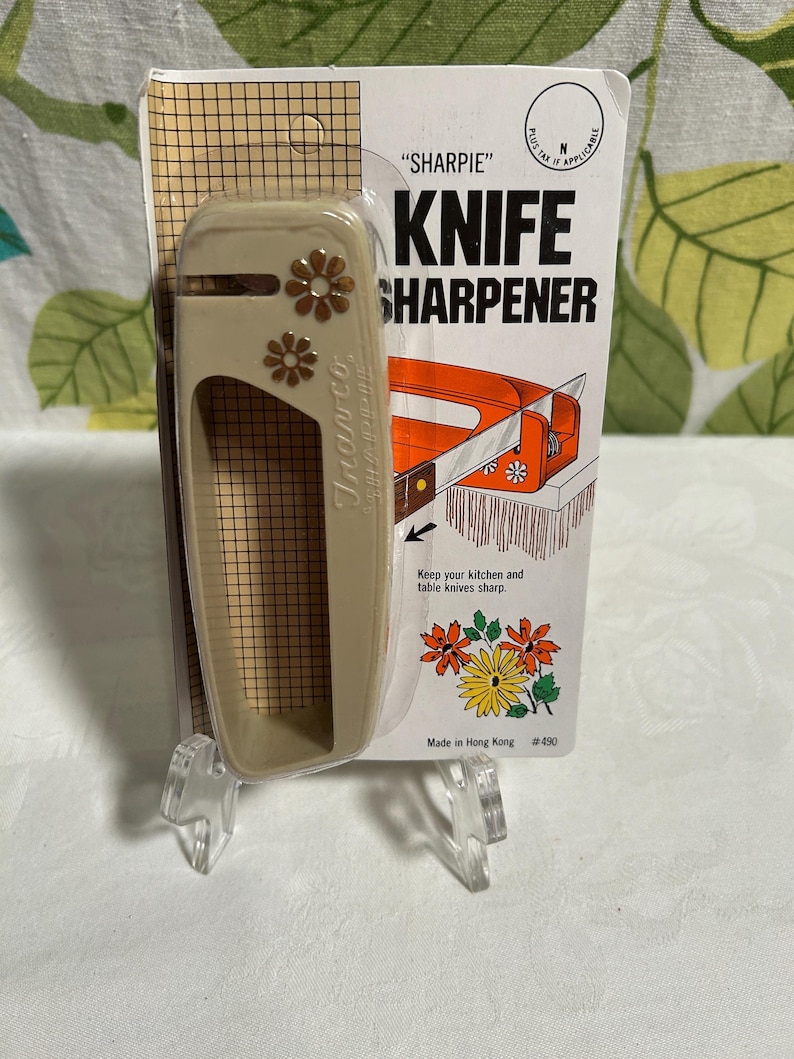 May include: A beige plastic knife sharpener with a floral design. The packaging says "SHARPIE" KNIFE SHARPENER and "Keep your kitchen and table knives sharp".