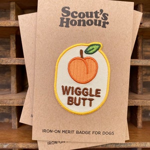 May include: Three brown paper cards with the text "Scout's Honour" printed in brown. Each card has an iron-on patch with a peach design and the words "Wiggle Butt". The patch is outlined in yellow and has a green leaf.