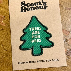 May include: A green felt patch shaped like a pine tree with the text "TREES ARE FOR PEES" in white. The patch is labeled "Scout's Honour IRON-ON MERIT BADGE FOR DOGS".