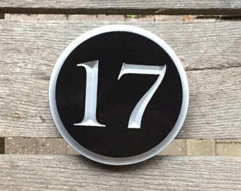 May include: A black and white round sign with the number 17 on it. The sign is attached to a wooden surface.