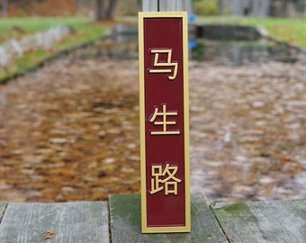 May include: A vertical wooden sign with a gold frame and a maroon background. The sign has three Chinese characters in gold lettering: "马 生 路".