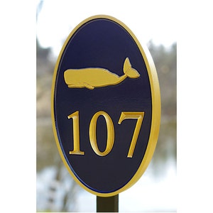 May include: A blue and gold oval sign with the number 107 and a gold whale silhouette. The sign is mounted on a wooden post.