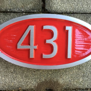May include: A red oval-shaped house number sign with a silver border and the number 431 in silver lettering.