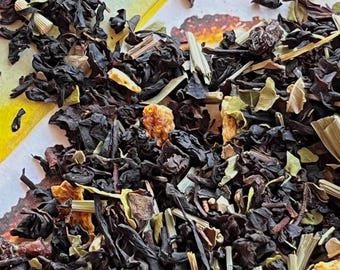 May include: Close-up of loose leaf tea blend with dark tea leaves, dried fruit pieces, and herbs. The blend includes orange and red pieces, along with green and tan herbs. The tea is a mix of textures and colors, perfect for a warm beverage.