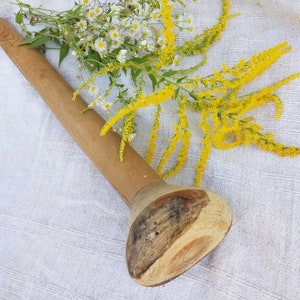 May include: A wooden rolling pin with a rounded end, lying on a white fabric surface with yellow flowers.