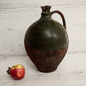 May include: A large, green and brown ceramic jug with a handle. The jug has a rustic, aged appearance.