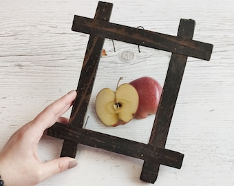 Könnte beinhalten: Ein brauner Holzrahmen mit dunkler Farbe liegt auf einer weißen Holzoberfläche. Im Rahmen befinden sich zwei rote Äpfel, einer ganz und einer halbiert.