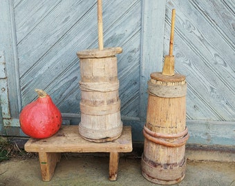 May include: Two wooden butter churns with wooden paddles, one on a wooden stool with a red gourd beside it. The churns are made of natural wood with a rustic finish.