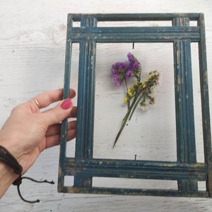 Könnte beinhalten: Ein blauer Holzrahmen mit dekorativem Design, der einen Strauß getrockneter Blumen mit violetten, weißen und gelben Blüten zeigt.