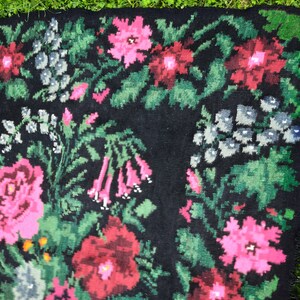 May include: A black rug with a floral pattern. The rug features pink, red, and green flowers on a black background.