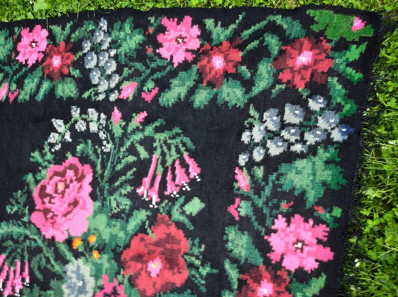 May include: A black rug with a floral pattern. The rug features pink, red, and green flowers on a black background.