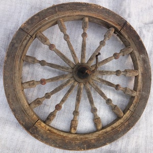 May include: A wooden spinning wheel with a large, circular frame and a central hub. The wheel has many spokes radiating outwards from the hub, and there are small wooden knobs at the ends of each spoke. The wheel is made of dark brown wood and has a rustic appearance.