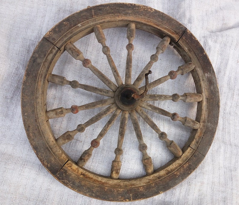May include: A wooden spinning wheel with a large, circular frame and a central hub. The wheel has many spokes radiating outwards from the hub, and there are small wooden knobs at the ends of each spoke. The wheel is made of dark brown wood and has a rustic appearance.