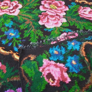 May include: A black wool rug with a floral pattern. The rug features pink, blue, and green flowers on a black background.