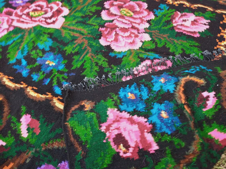May include: A black wool rug with a floral pattern. The rug features pink, blue, and green flowers on a black background.
