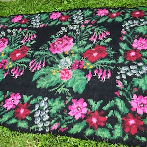 May include: A black rug with a floral pattern. The rug features pink, red, and green flowers on a black background.