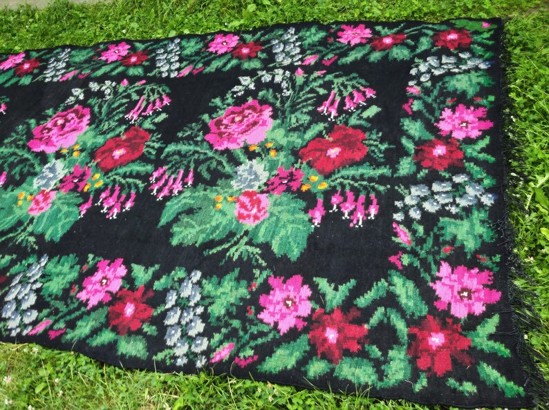 May include: A black rug with a floral pattern. The rug features pink, red, and green flowers on a black background.