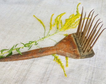 Könnte beinhalten: Ein Holzkamm mit Metallzähnen, der zum Kämmen von Wolle verwendet wird. Der Kamm liegt auf einer weißen Stoffoberfläche mit gelben Blumen.