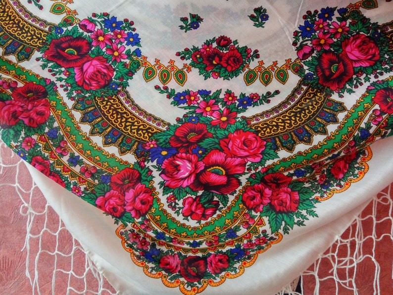 K&ouml;nnte beinhalten: Ein wei&szlig;er Stola aus Stoff mit einem bunten Blumenmuster. Das Muster zeigt rote, rosa, blaue und gr&uuml;ne Blumen mit goldenen Akzenten. Der Stola hat einen Fransenrand.