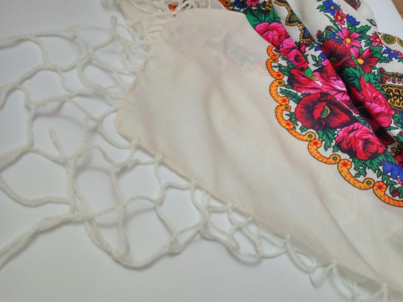 K&ouml;nnte beinhalten: Ein wei&szlig;er Baumwollschal mit einem bunten Blumenmuster und einem wei&szlig;en H&auml;kelrand.
