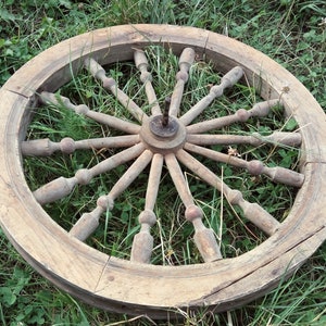 May include: A large, wooden spinning wheel with a circular frame and spokes radiating from the center. The wheel is weathered and has a natural wood finish.