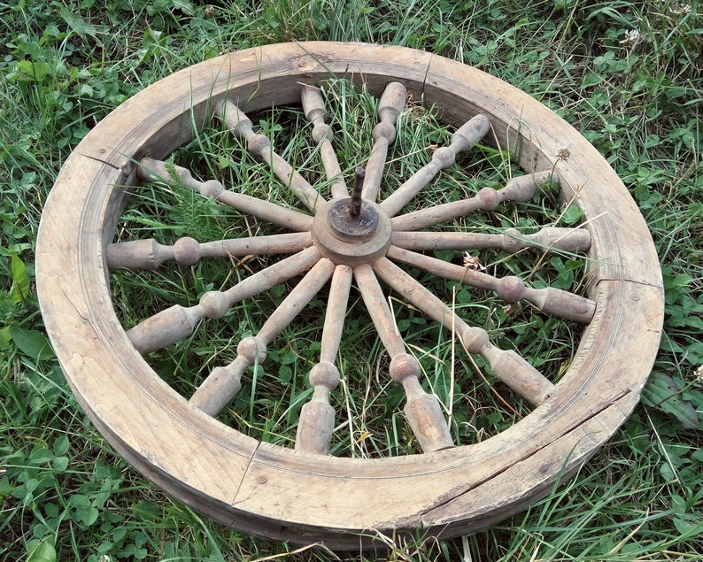 May include: A large, wooden spinning wheel with a circular frame and spokes radiating from the center. The wheel is weathered and has a natural wood finish.
