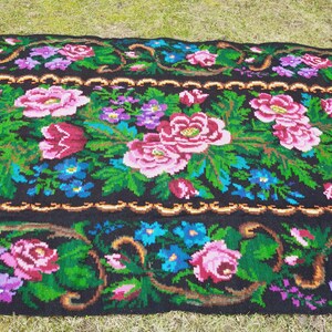 May include: A black wool rug with a floral pattern featuring pink, red, green, blue, and purple flowers. The rug has a gold border.